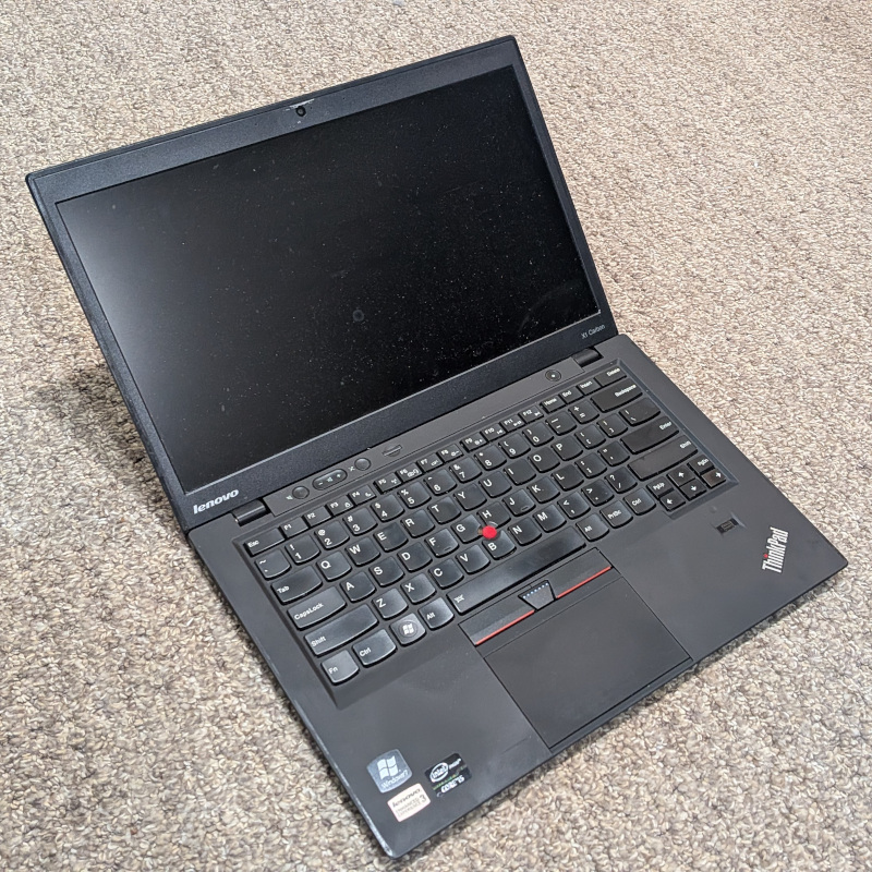 a black laptop sitting on a carpeted floor; the laptop is opened but the screen is turned off