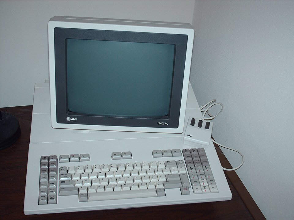 a 1980s computer system, with green monitor on top of a white computer body, with keyboard and 3-button mouse