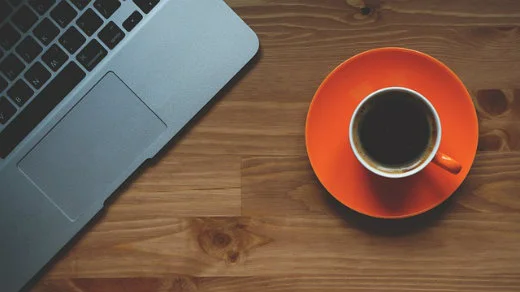 A cup of coffee on an orange saucer next to a laptop